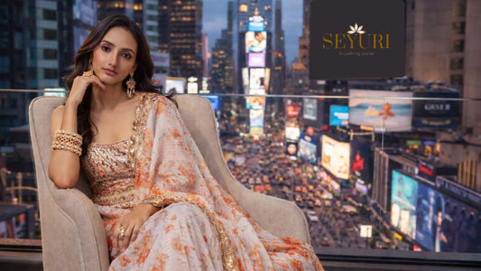 Woman in a peach floral embroidered saree sitting on a modern chair with Times Square city lights and a SeYuri billboard in the background.
