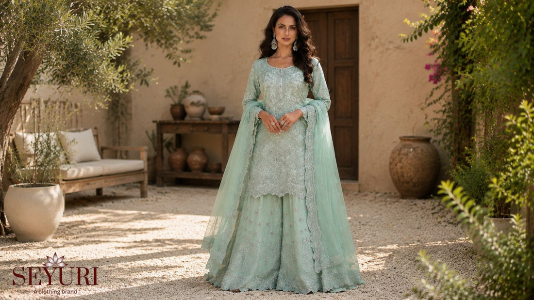 A woman in a mint green embroidered traditional outfit posing in a sunlit courtyard fashion photoshoot.