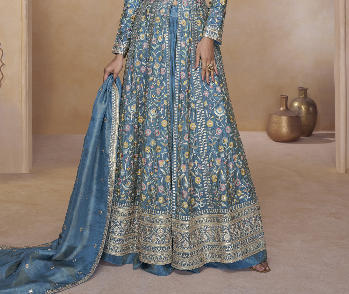 Blue Embroidered Floor-Length Gown with Detailed Floral Work, Long Sleeves, and Matching Dupatta Worn by a Woman at a Royal Backdrop.
