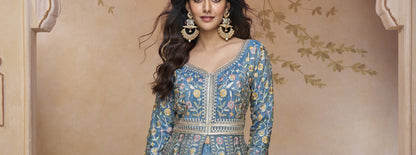 Blue Embroidered Floor-Length Gown with Detailed Floral Work, Long Sleeves, and Matching Dupatta Worn by a Woman at a Royal Backdrop.