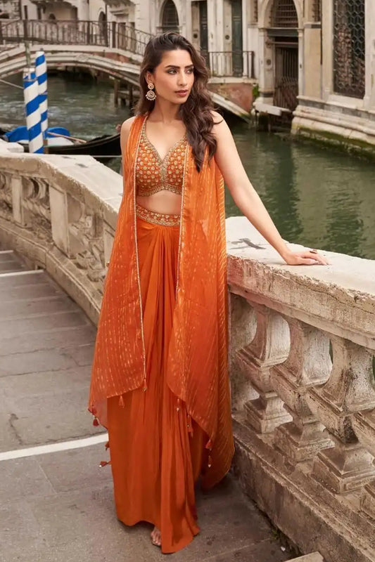 Woman in an orange traditional outfit standing on a stone bridge over a canal with gondolas in the background.