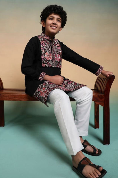 Child wearing a traditional outfit with a floral design sitting on a wooden bench.