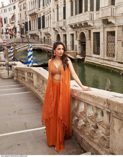 Woman in an orange traditional outfit standing on a stone bridge over a canal with historic buildings in the background.