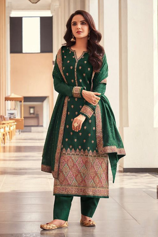 Woman in a green traditional outfit with intricate patterns standing indoors.