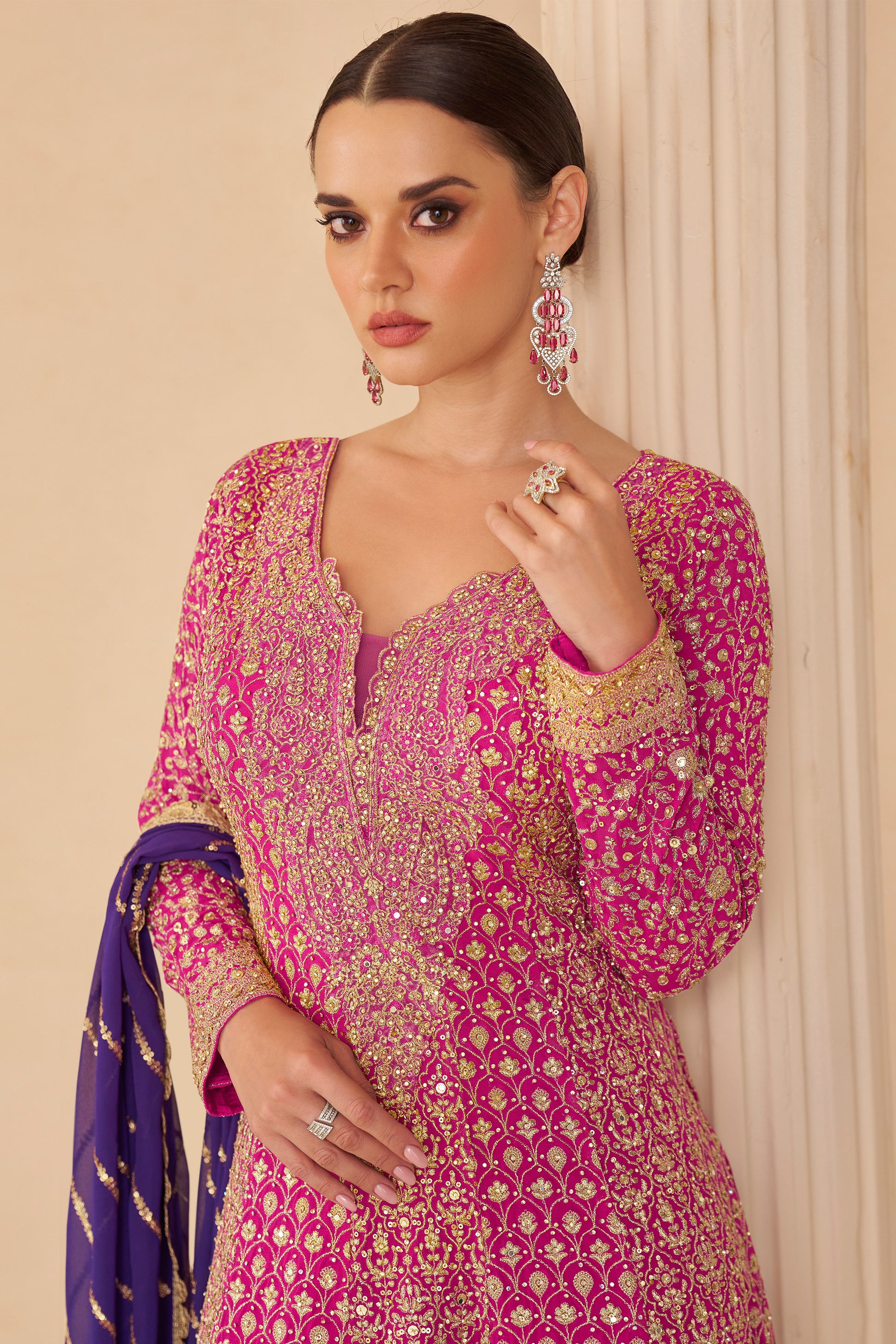 Woman wearing a pink and gold embroidered traditional outfit with a purple dupatta.