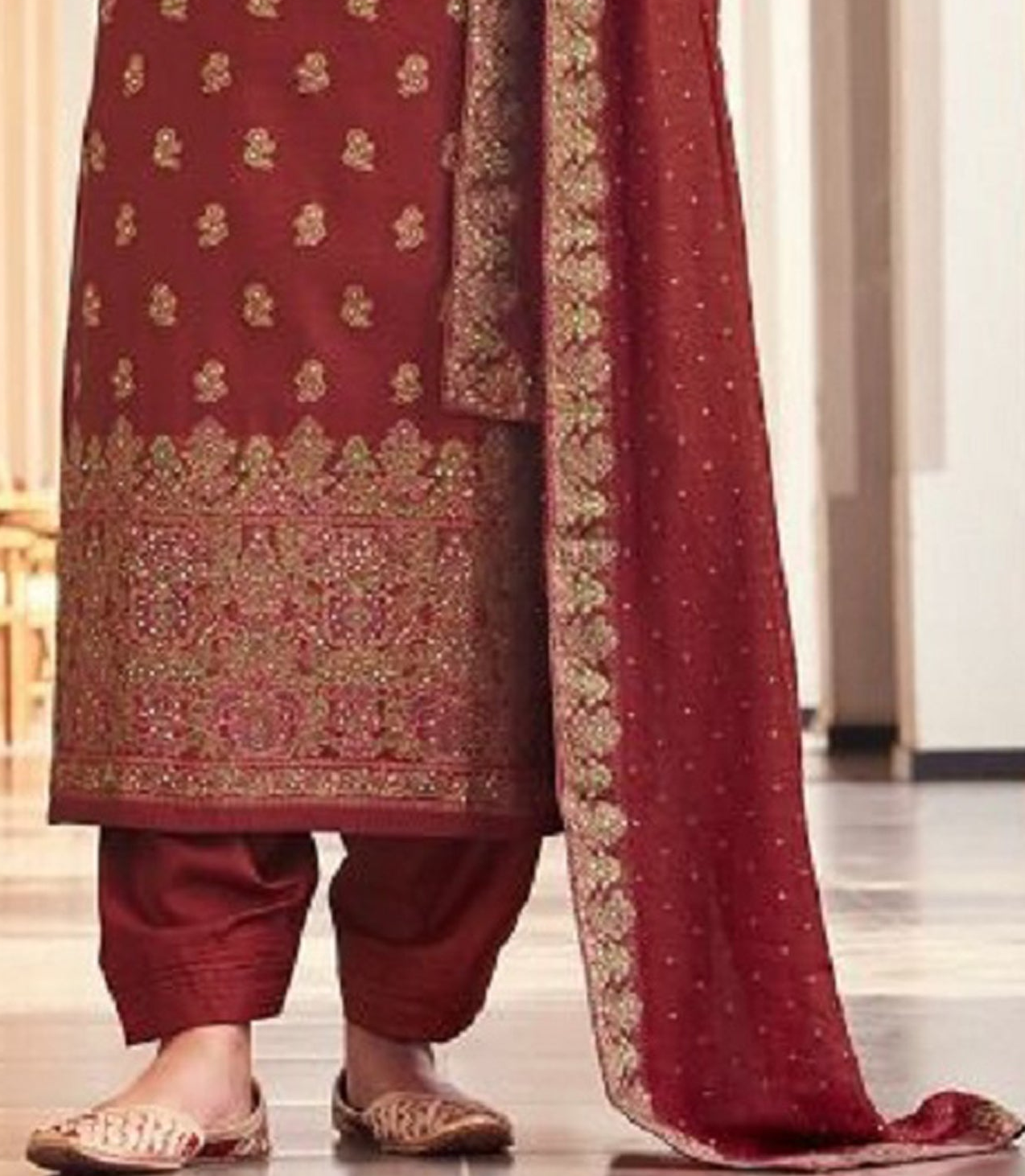 Woman in a red traditional outfit with gold patterns in an indoor setting.