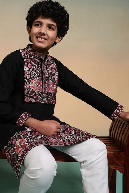 Child wearing a traditional embroidered kurta with white pants, sitting on a wooden bench.