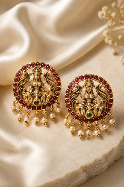 Close-up of sculpted gold-tone earrings framed with deep red stones and pearl-like drops
