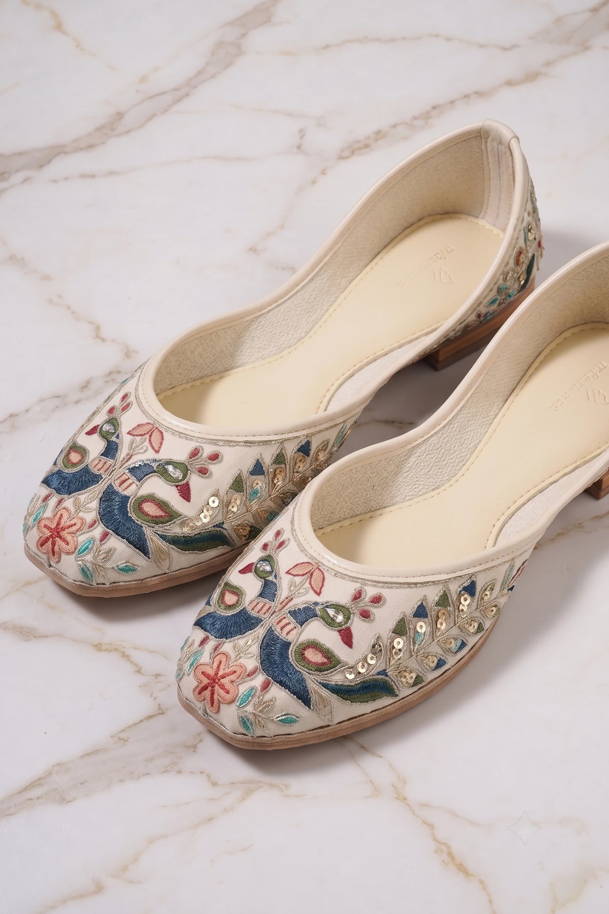 Close-up of embroidered peacock design with colorful threadwork on cream jutti