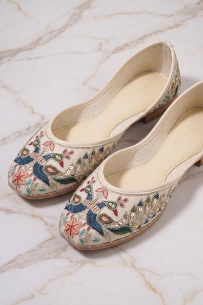 Close-up of embroidered peacock design with colorful threadwork on cream jutti