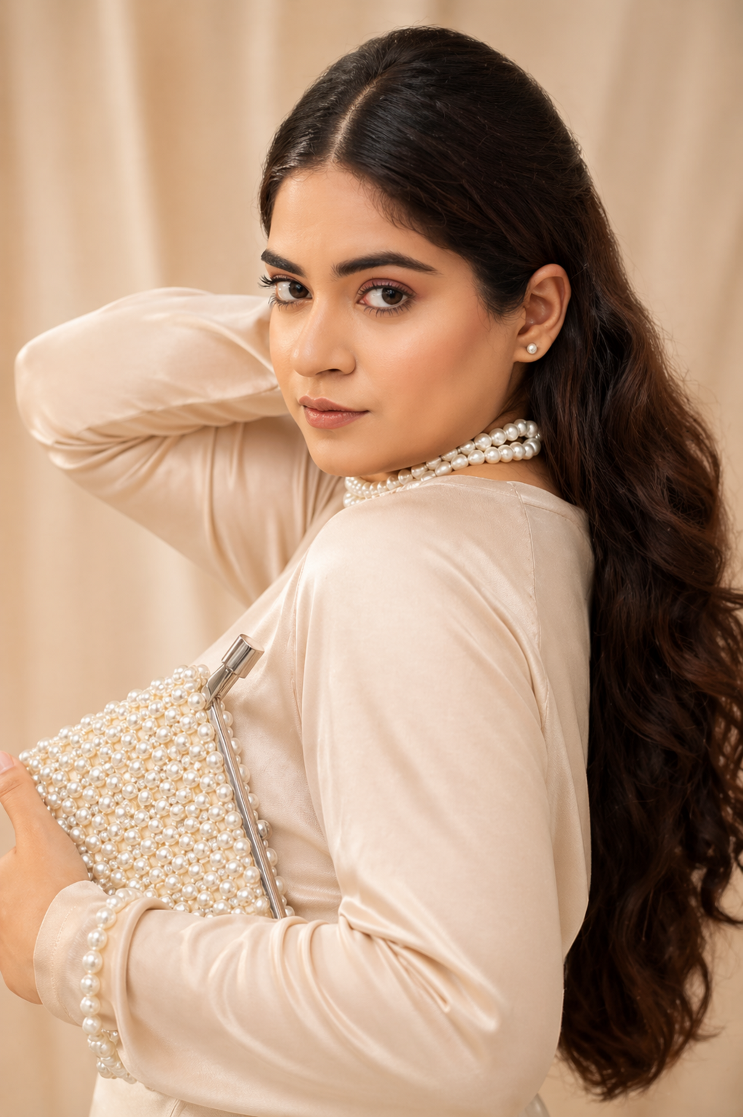 Woman wearing a beige outfit with pearl details against a beige background