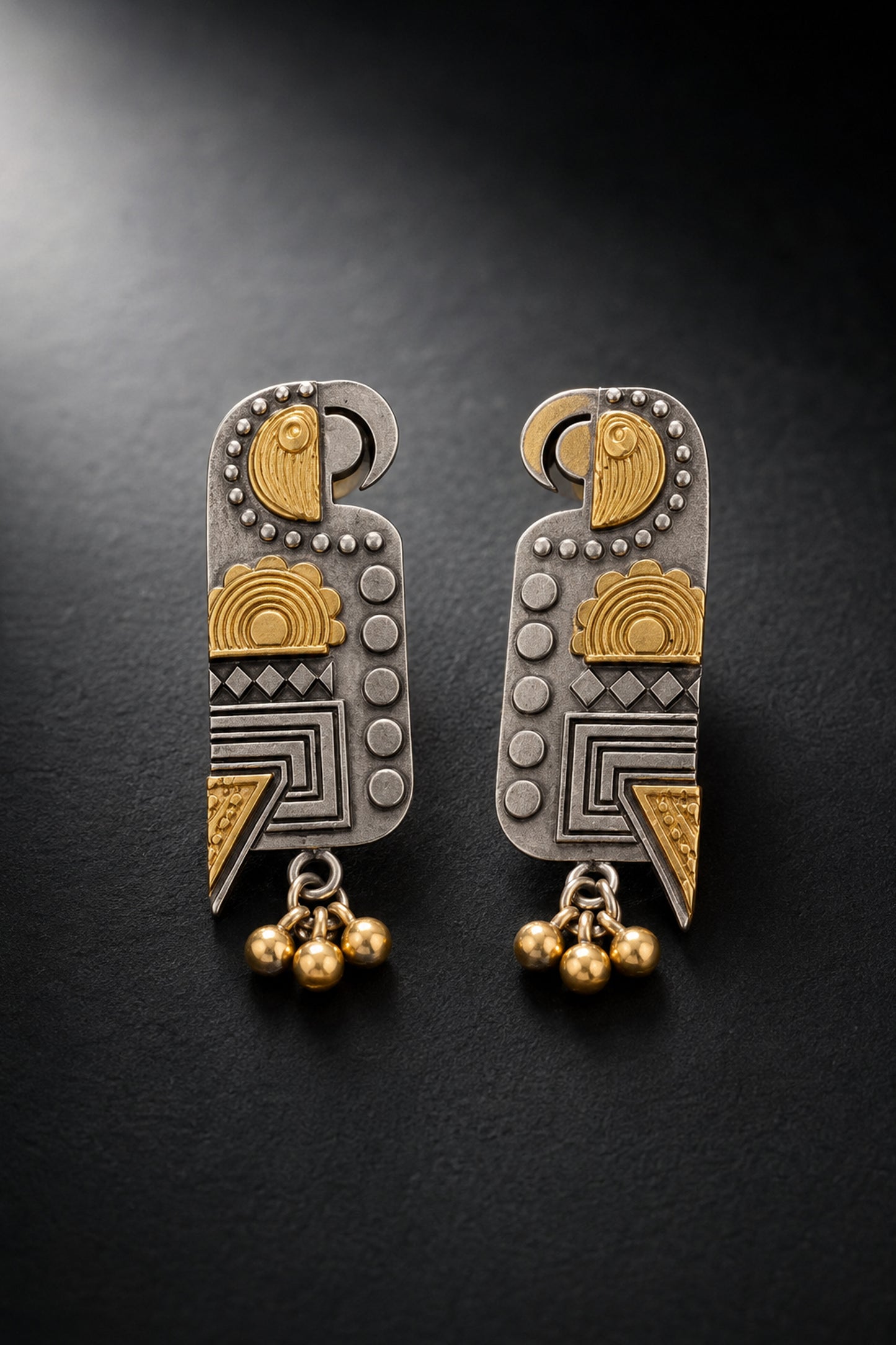 Mixed silver-tone and gold-tone geometric drop earrings on charcoal