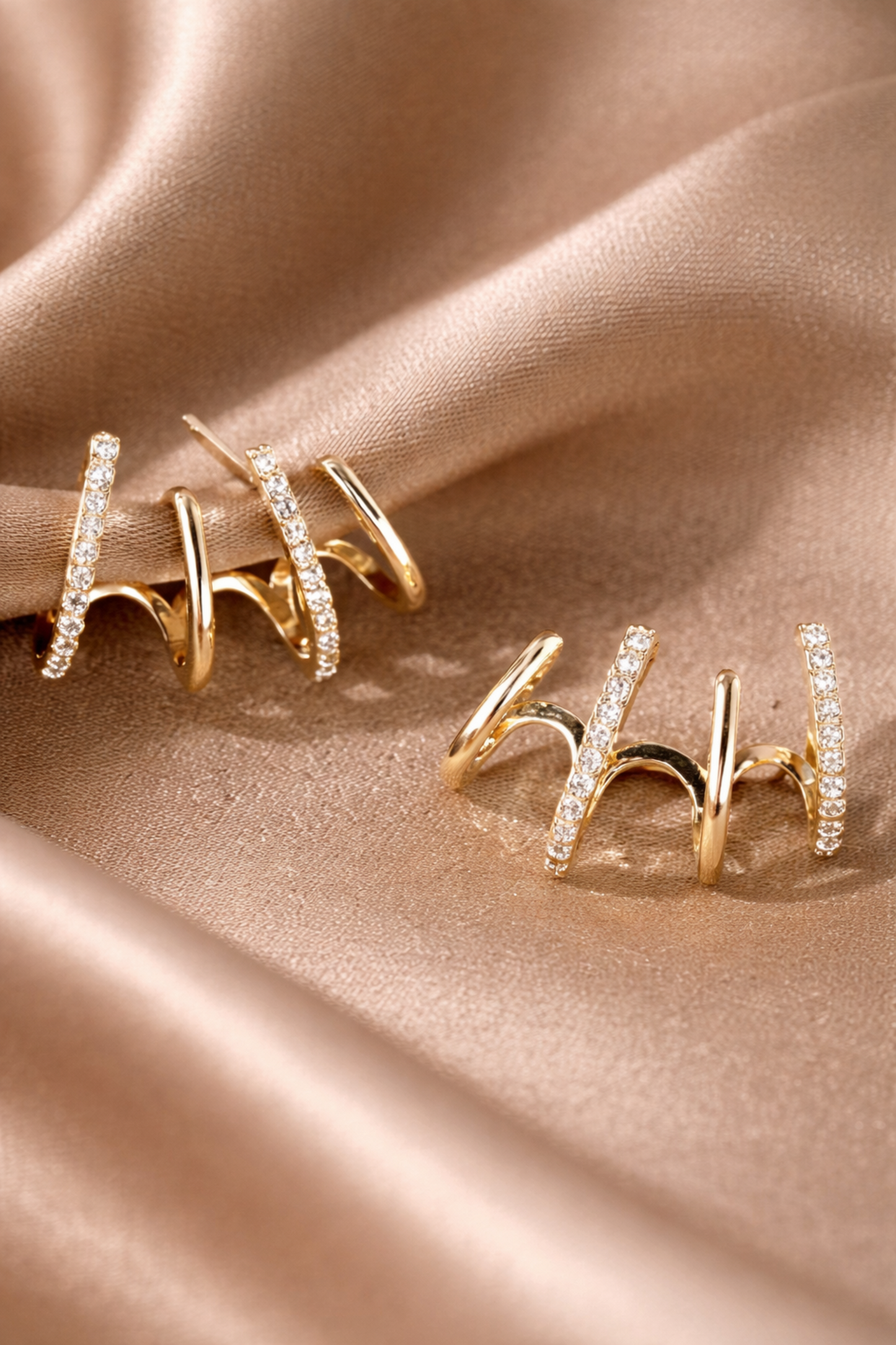 Gold ear climber earrings with zircon stones on satin fabric background