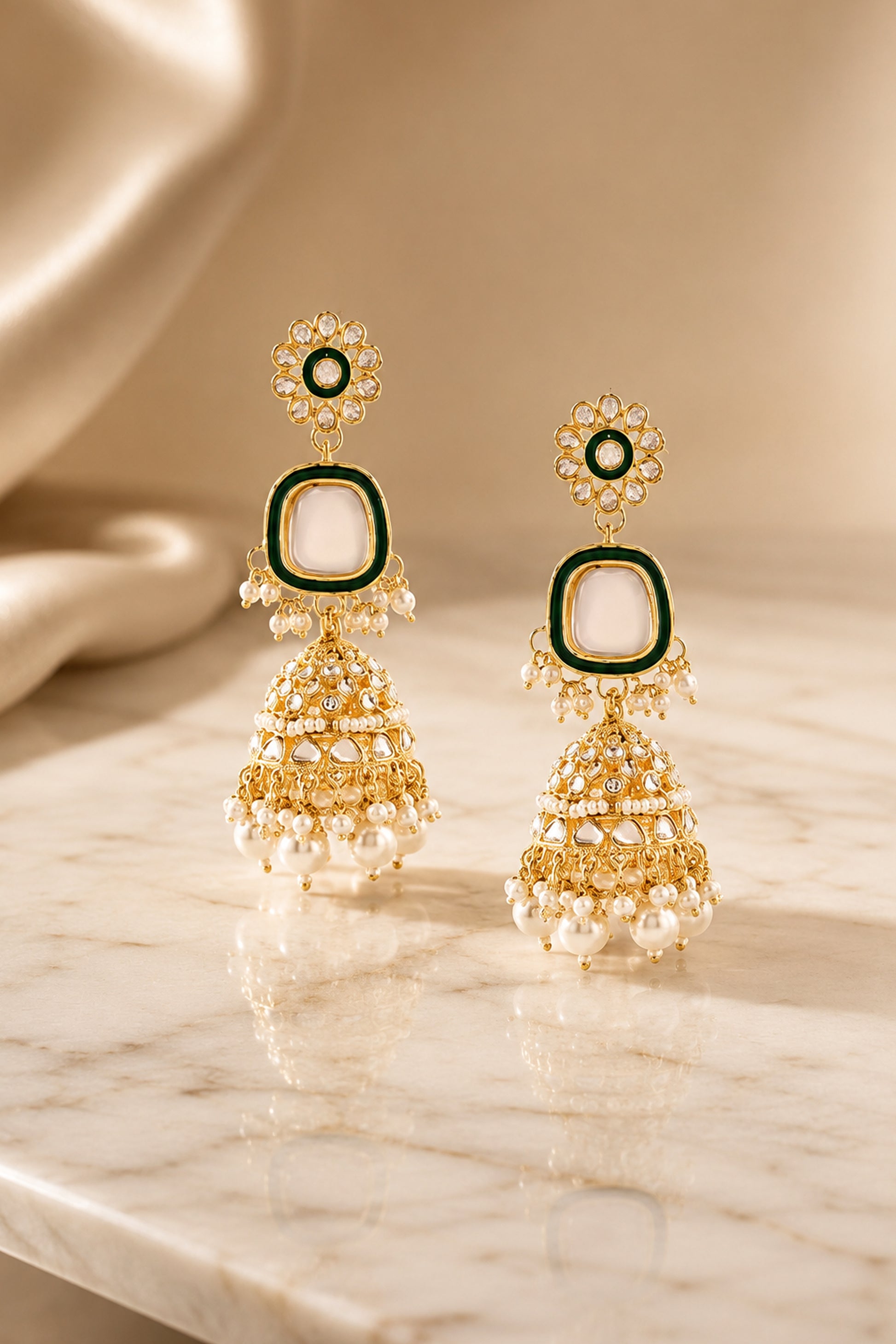 Gold-tone long jhumka earrings with green framing, clear reflective stones and pearl-like drops.