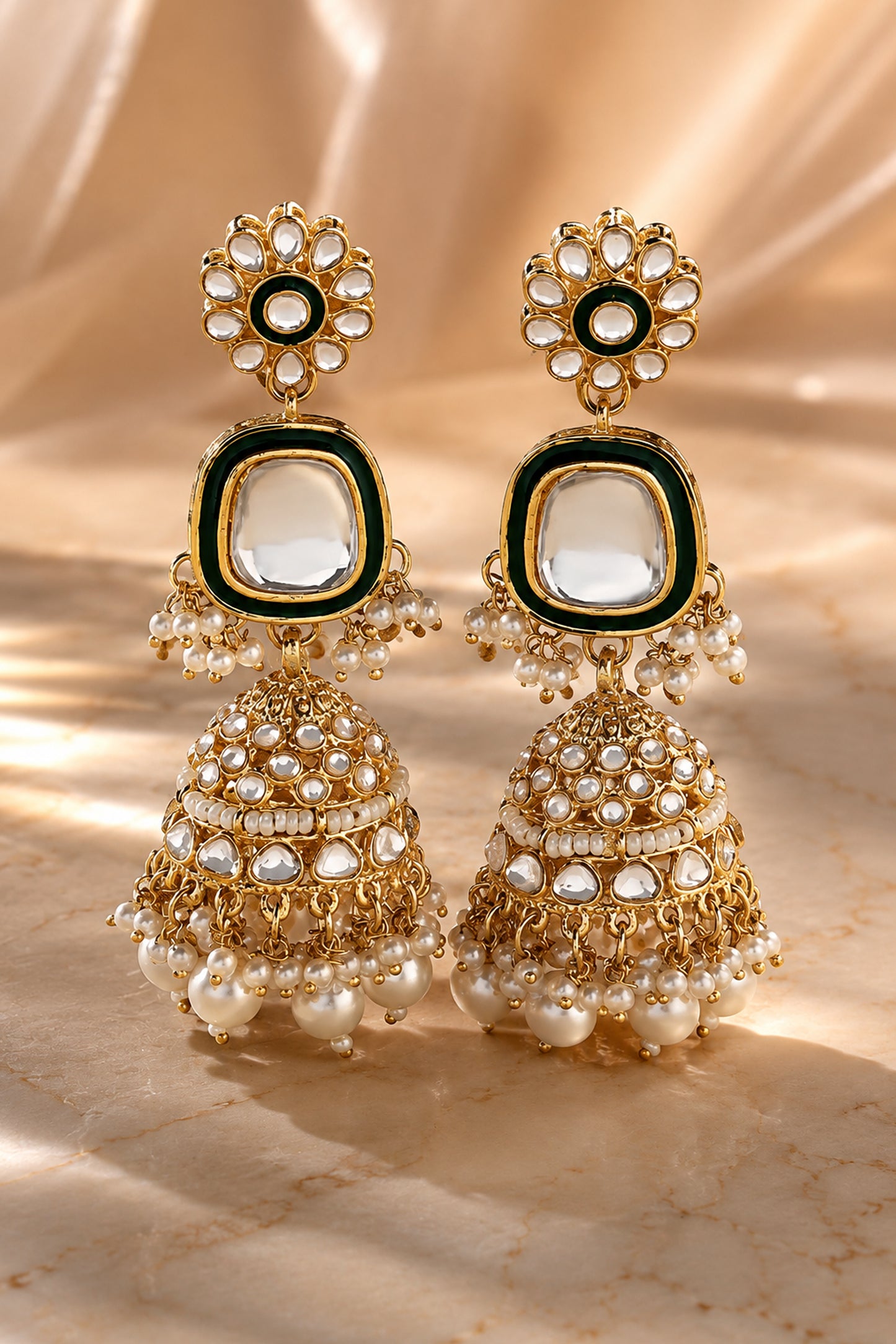 Gold-tone drop earrings photographed on champagne fabric with clear reflective stone accents.