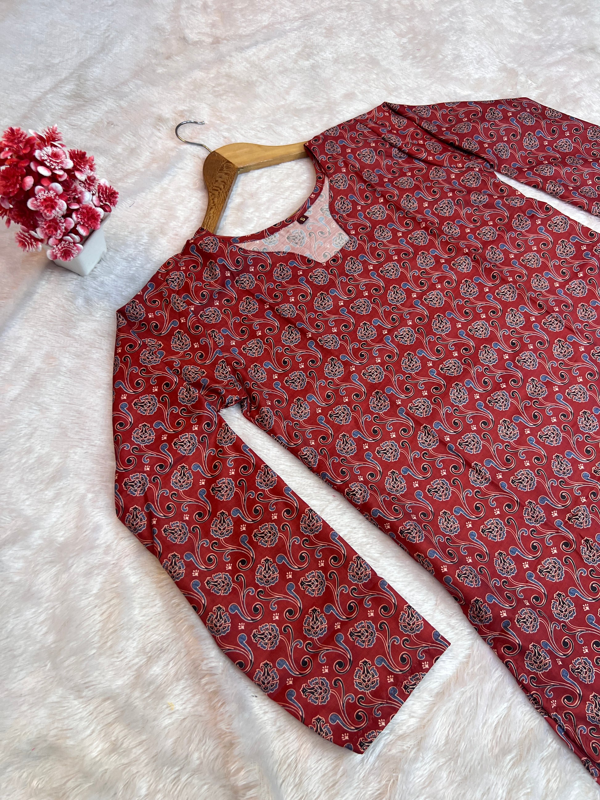Maroon patterned shirt on a white surface with a hanger and floral decoration.