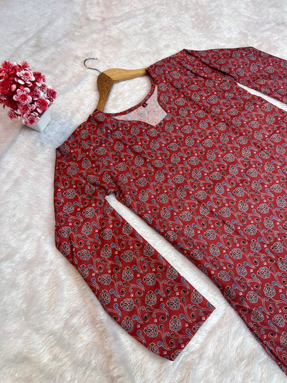 Maroon patterned shirt on a white surface with a hanger and floral decoration.