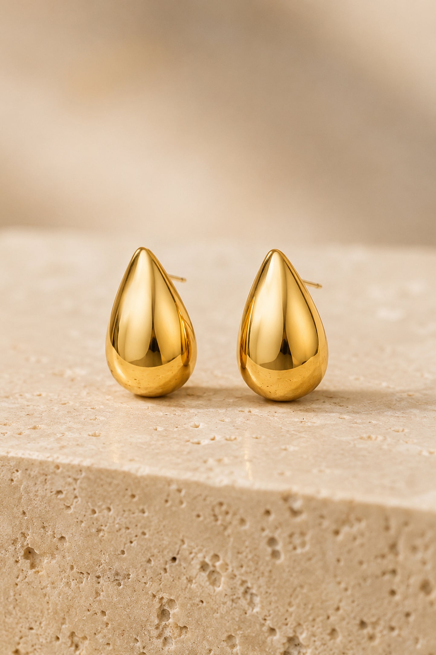 Polished teardrop earrings displayed on textured travertine