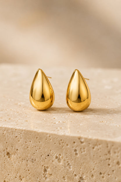 Polished teardrop earrings displayed on textured travertine