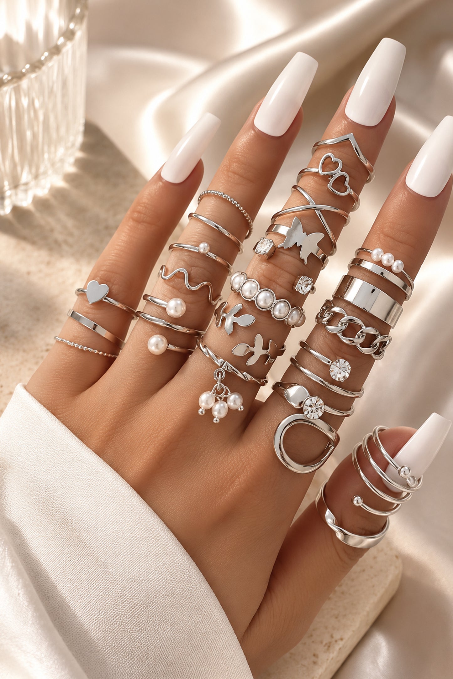 Mixed polished rings styled across a hand with white nails
