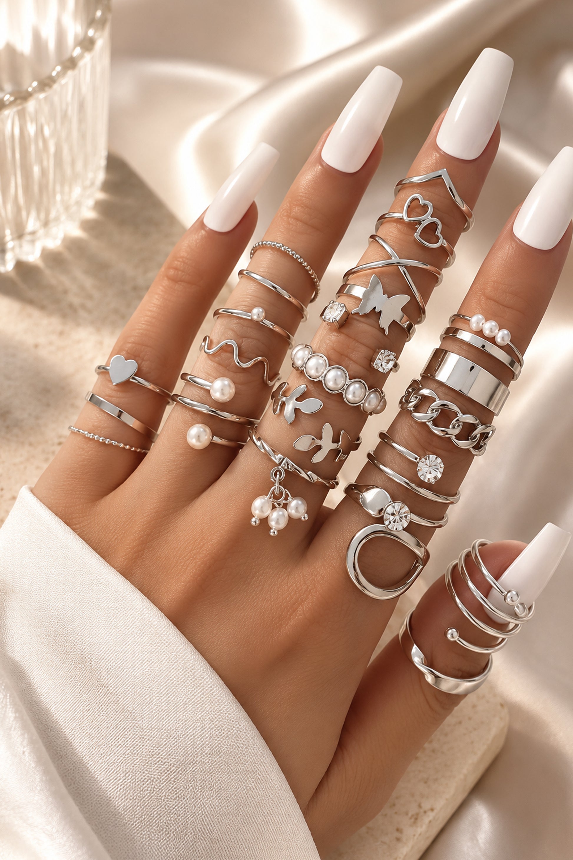 Mixed polished rings styled across a hand with white nails