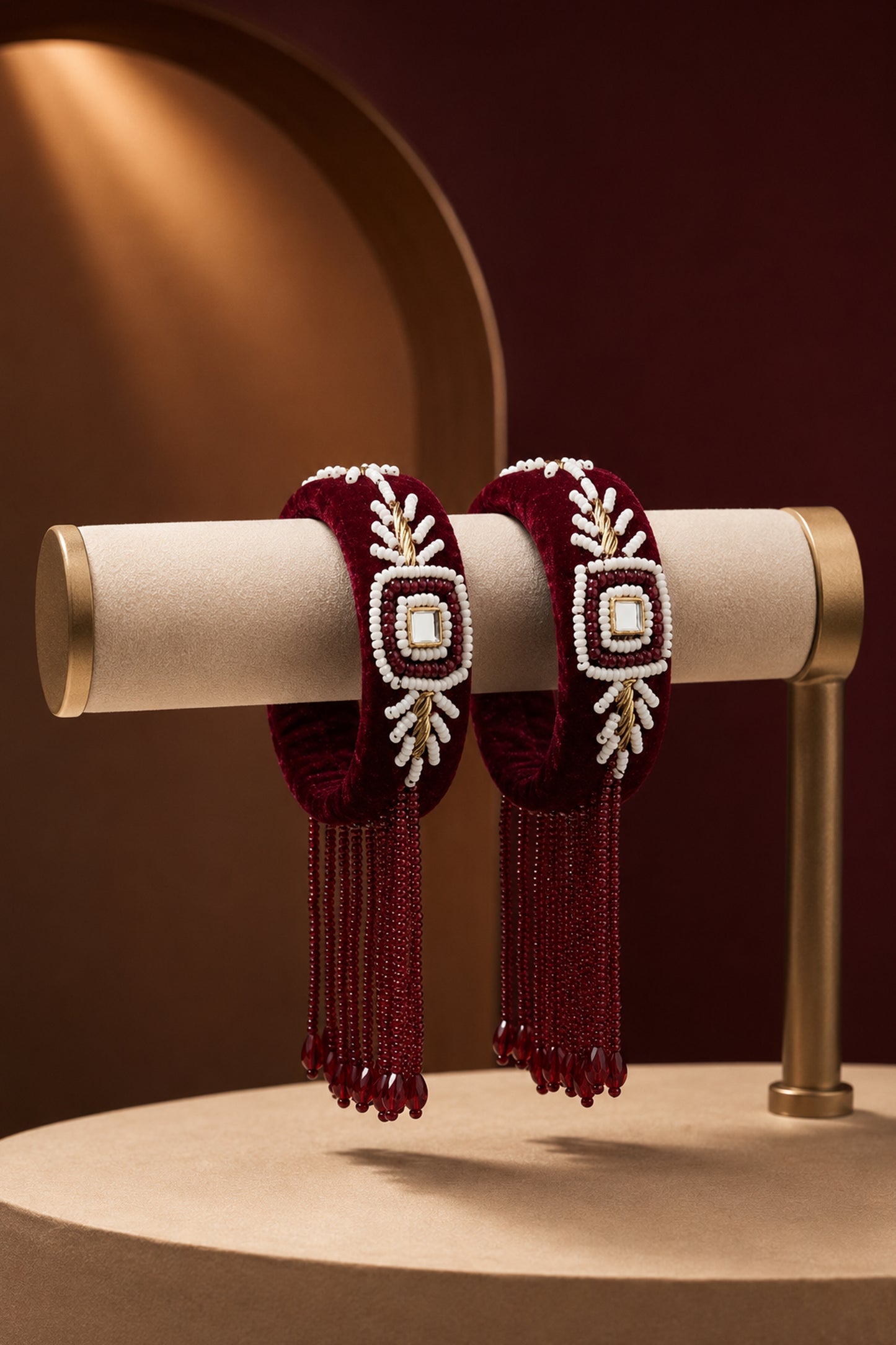 Pair of velvet bangles with maroon bead fringe on a cream display