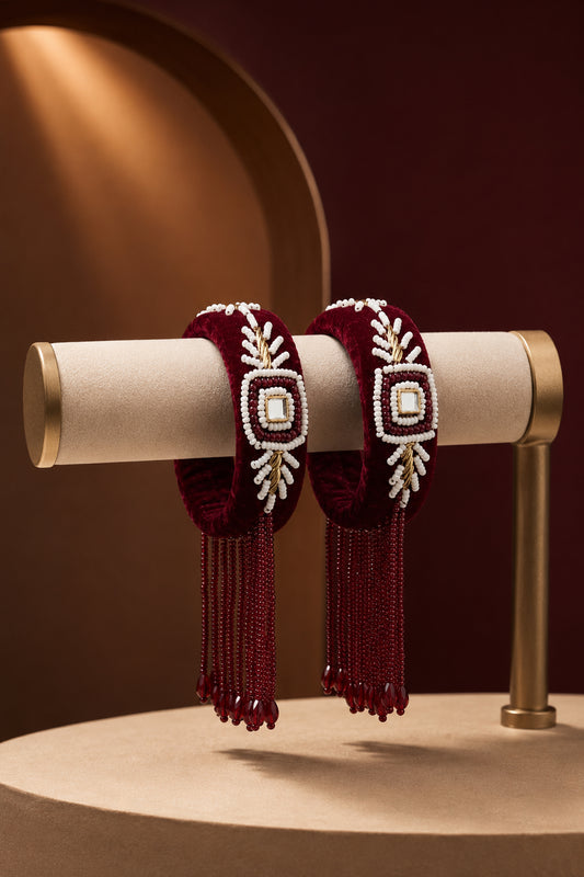Pair of velvet bangles with maroon bead fringe on a cream display
